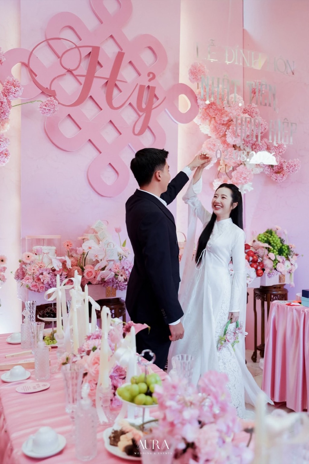 Cô dâu chú rể khiêu vũ trước chữ Hỷ, bảng tên kết hoa và bàn lễ hồng phấn
