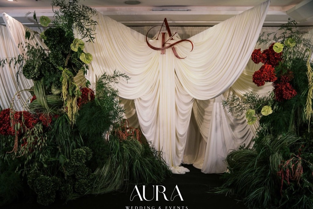 Backdrop chụp ảnh lụa trắng ngà xếp nếp, monogram AK đỏ và hai khối cây xanh điểm hoa đỏ