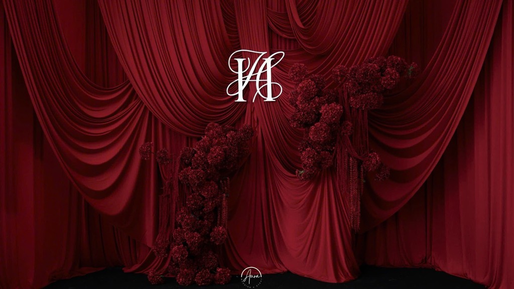Toàn cảnh backdrop vải nhung đỏ buông tầng, monogram trắng và hai trụ hoa đỏ thẫm