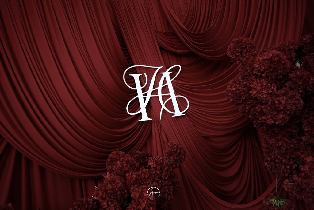 Monogram trắng giữa những lớp vải nhung đỏ xếp võng và các cụm hoa đỏ