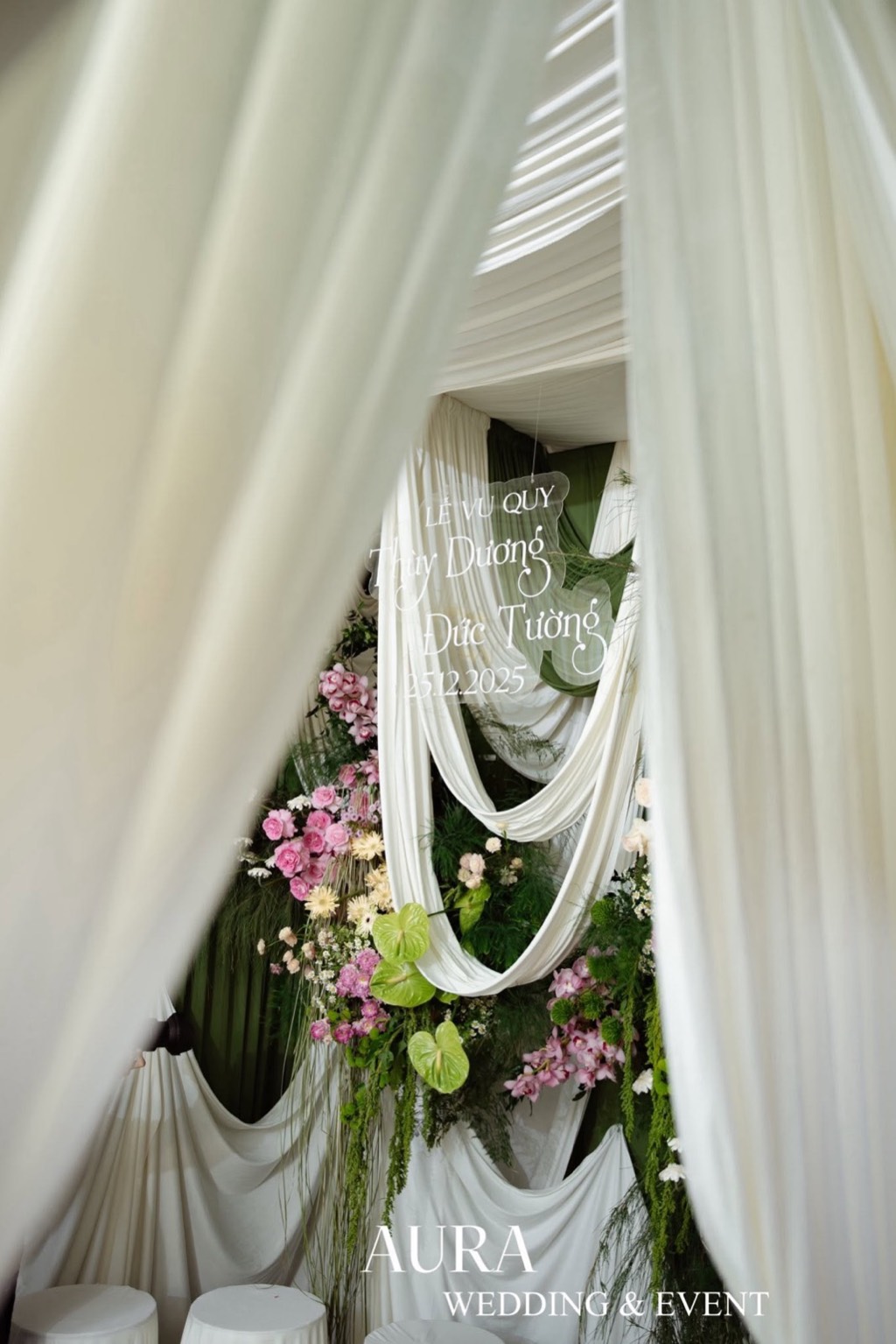 Lễ đường nhìn qua những lớp voan trắng rủ, bảng tên mica treo giữa các vòng vải và hoa hồng